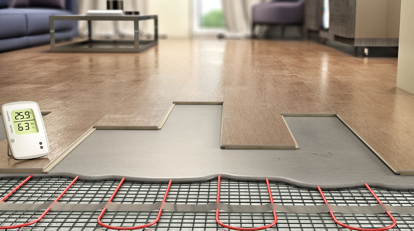 Vue plongeante sur chantier de plancher chauffant montrant réseau de tubes noirs disposés en serpentin sur panneaux isolants blancs-gris avec fixations, outils de pose au premier plan